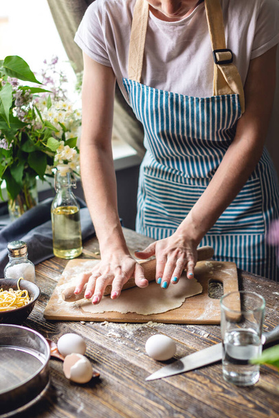 Жінка розкачує свіже тісто для приготування макаронних виробів у затишній атмосфері. Концепція приготування смачної їжі в домашніх умовах
 - Фото, зображення