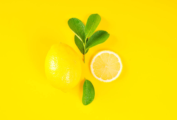 Lemons and green leaves on bright yellow background. Lemon background concept, flat lay. Lemon fruit, citrus minimal concept. Creative background made of lemon and leaf. Top View. - Photo, Image