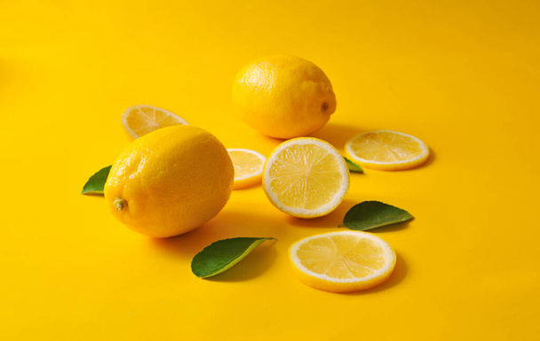Lemons and green leaves on bright yellow background. Food concept, flat lay. Lemon fruit, citrus minimal concept, vitamin C. Creative background made of lemon and leaf. - Фото, изображение