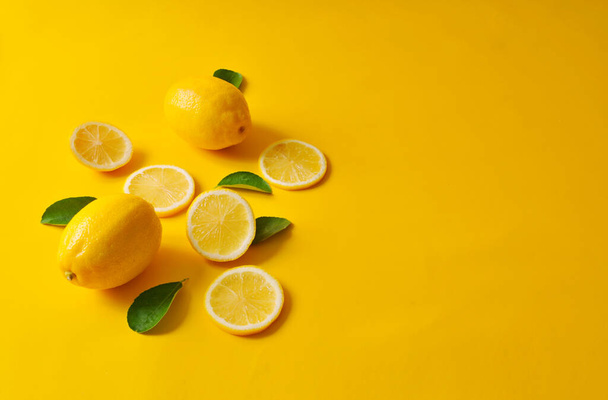Lemons and green leaves on bright yellow background. Food concept, flat lay. Lemon fruit, citrus minimal concept, vitamin C. Creative background made of lemon and leaf. - Photo, Image
