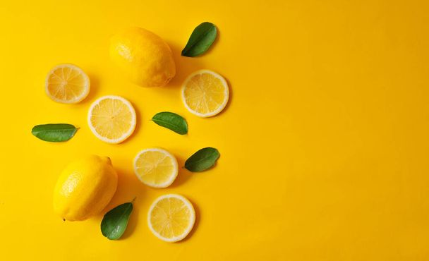 Lemons and green leaves on bright yellow background. Food concept, flat lay. Lemon fruit, citrus minimal concept, vitamin C. Creative background made of lemon and leaf. Top View. - 写真・画像