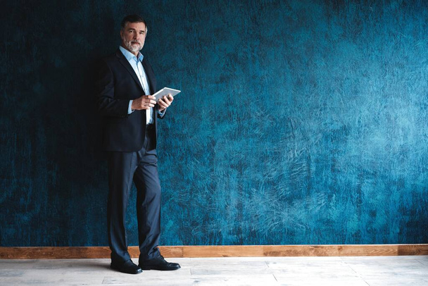 Happy mature businessman working with modern tablet isolated on dark blue background. - Foto, Bild