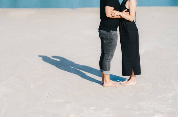 pareja joven un chico con una chica en ropa negra están caminando sobre la arena blanca en el borde del agua azul
 - Foto, Imagen