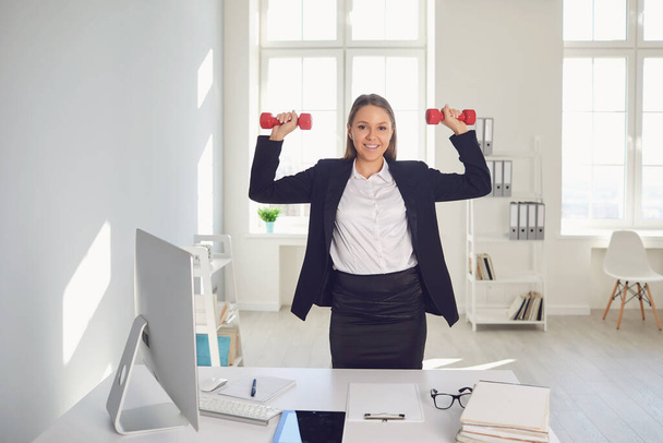 Businesswoman is doing exercises with dumbbells in the office during the break. - Fotografie, Obrázek