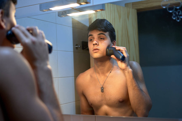 boy shaving with electric machine in mirror - Φωτογραφία, εικόνα