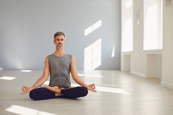 Yoga man. Bearded guy is practicing yoga in a lotus position sitting in a studio - Foto, imagen