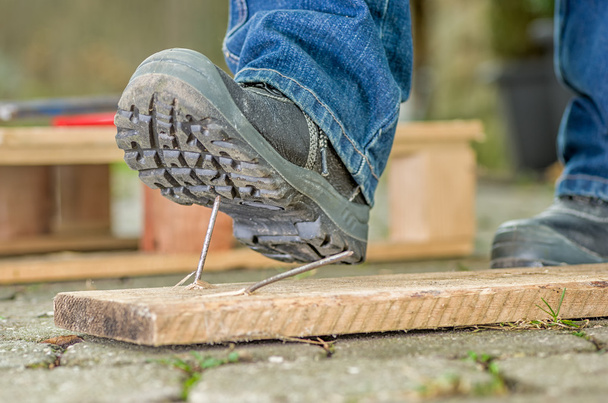 werknemer met veiligheid laarzen stappen op een nagel - Foto, afbeelding