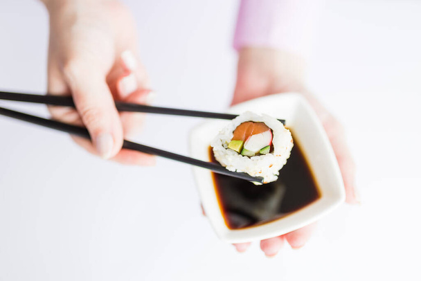 Close up of woman holding bowl with soy sauce and chopsticks with sushi roll, japanese traditional healthy meal concept. - Foto, afbeelding