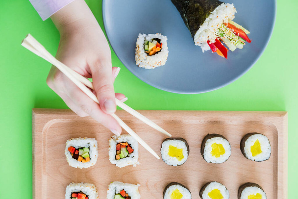 Flat lay of female hand using chopsticks for eating sushi rolls set. - Photo, Image