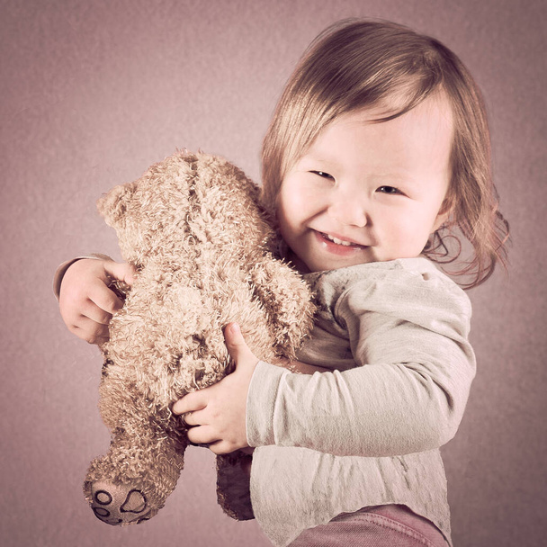 linda poco alegre mixta raza asiática bebé chica en su mano ella lleva un osito de peluche marrón color, suave tonificado
 - Foto, Imagen