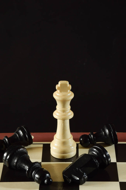 A sakktábla egy fehér alakja a király, és körülötte fekszenek a fekete darabok, amiket legyőzött.. - Fotó, kép