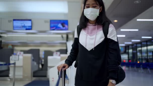 Nuori ruskea iho Aasian nainen suojaava lääketieteellinen naamio kävelee jonossa jonossa lentokentän terminaalin lähtöaulassa, matkustaa kotiin, covid-19 pandemia, uusi normaali sosiaalinen etäisyys, hidastettu     - Materiaali, video