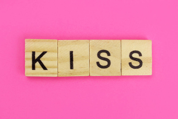 woord kus gemaakt van houten letters op een roze achtergrond - Foto, afbeelding