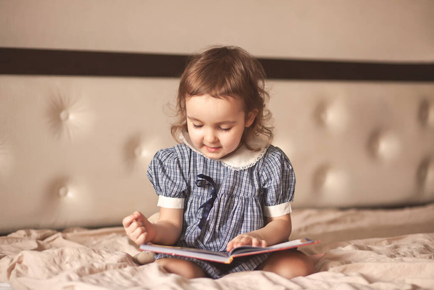 Small cute girl in a retro dress reading a book. - Foto, afbeelding