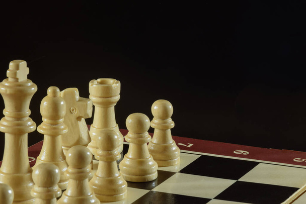 Na levé straně šachovnice jsou různé bílé šachové figurky ze dřeva. Za figurkou je černé pozadí. - Fotografie, Obrázek
