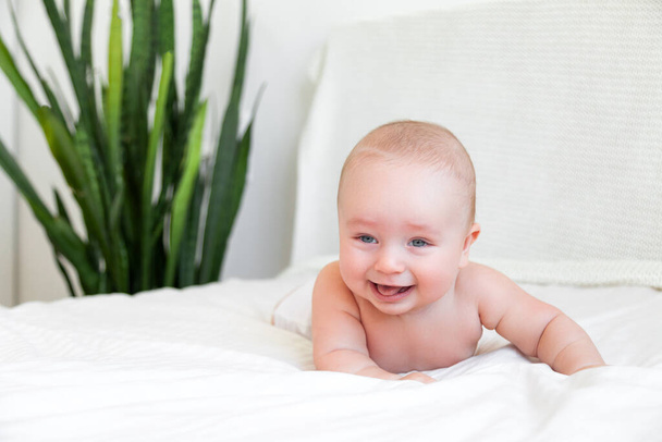 Beautiful baby playing with legs in white bedroom on white background - Foto, afbeelding