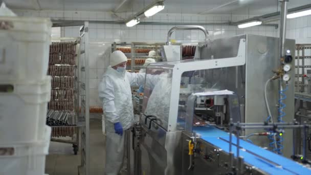 Makkaraosaston työntekijä seisoo lähellä automaattista laitetta makkaroiden pakkaamiseksi tyhjiöpakkaukseen. - Materiaali, video
