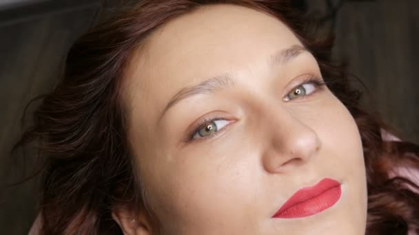 Ritratto di una bella giovane donna prima del trucco permanente microblading con il tatuaggio del sopracciglio e labbra con rossetto rosso si trova su un divano in un salone di bellezza
 - Filmati, video