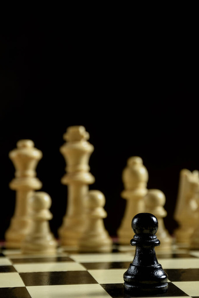 En un tablero de ajedrez en primer plano hay una pieza de ajedrez negro Peón. Detrás de ella hay una fila de formas blancas borrosas
. - Foto, Imagen