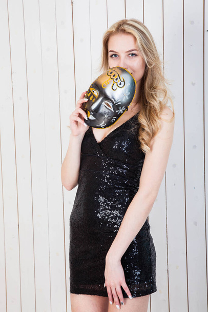 blonde girl in a black short dress stands with an actor's mask on her head - Foto, afbeelding