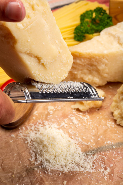 Άνδρας που μαγειρεύει με σκληρό ιταλικό τυρί, τριμμένη παρμεζάνα ή gra padano τυρί, χέρι με τρίφτη τυριού - Φωτογραφία, εικόνα