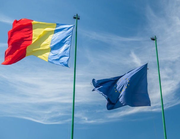 Romanya ulusal bayrağı ve Avrupa Birliği bayrağı açık mavi gökyüzüne doğru dalgalanıyor. - Fotoğraf, Görsel