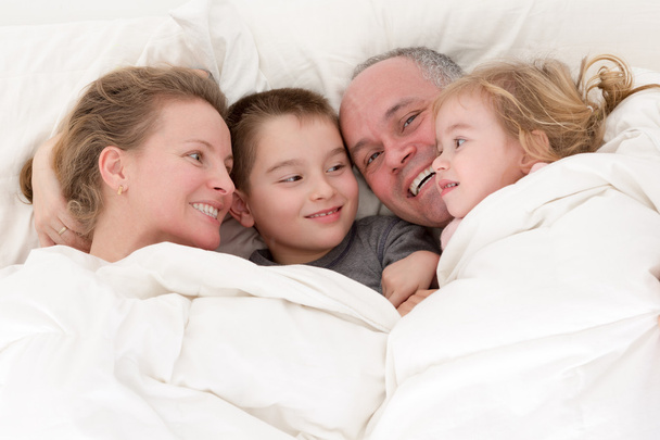 Happy young family cuddling together in bed - Photo, Image