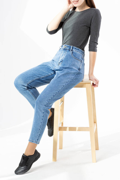 girl in jeans sitting on a wooden bench showing jeans on a white background close-up, blue jeans - Foto, Imagen