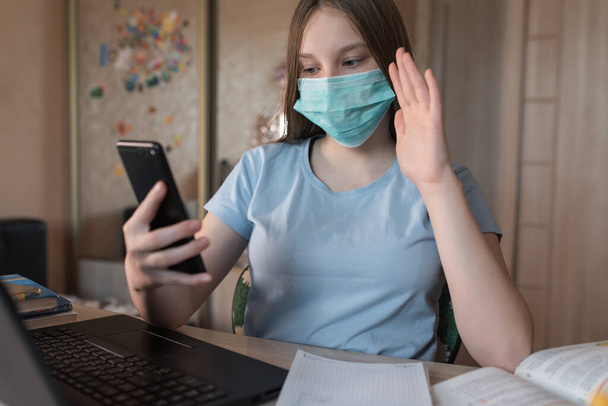 Teenager girl, in a medical mask, protection bacteria of viruses and diseases, makes a video call on a smartphone, e-education and Internet lessons, distance learning. Video training on the Internet. - Foto, Imagen
