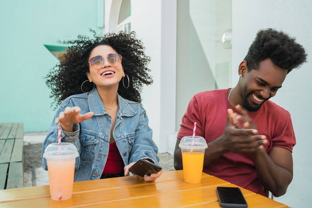 Portrait of two Afro friends having fun together and enjoying good time while drinking fresh fruit juice outdoors at cafeteria. - Фото, зображення