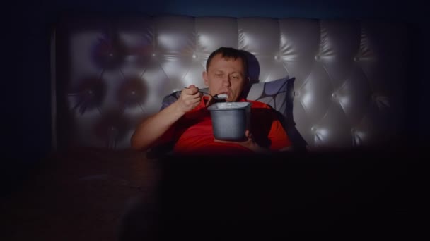 Ein netter Kerl genießt einen Abend vor dem Fernseher mit einem leckeren Eis - Filmmaterial, Video