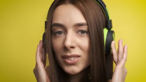 Portrait of a cute girl on a yellow background in stylish green headphones who listens to music and smiles at the camera. Active lifestyle - Imágenes, Vídeo
