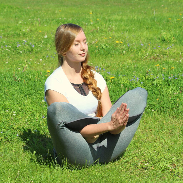 Young woman of European appearance does yoga in summer nature. Woman sitting in flowering lotus pose, vikasitakamalasana. High quality photo for web and print with empty space for text and design. - Fotó, kép