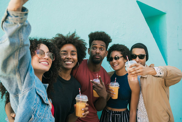 Portrait of multi-ethnic group of friends having fun together and taking a selfie while drinking fresh fruit juice.  - Foto, imagen
