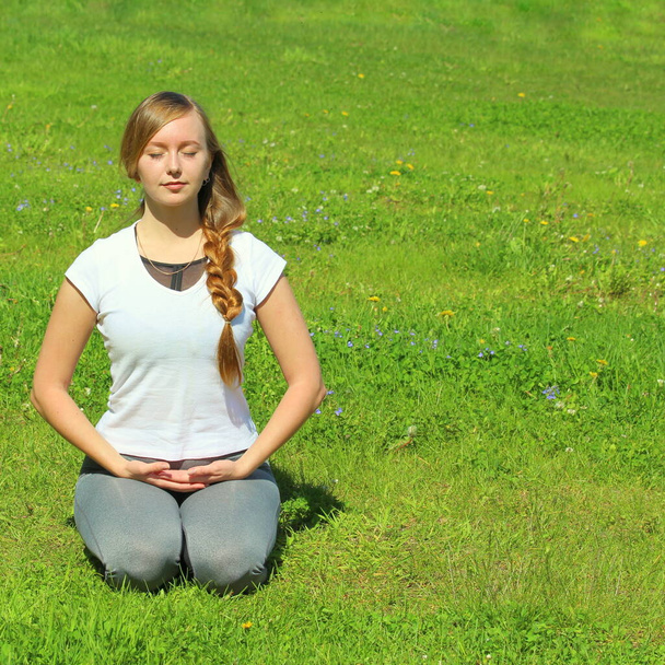 Young woman of European appearance does yoga in summer nature. Woman sitting on her knees in vajrasana, thunderbolt pose. High quality photo for web and print with empty space for text and design. - Foto, Imagem