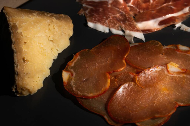A closeup shot of thin-sliced raw pork meat with a pie on a black plate - Fotó, kép