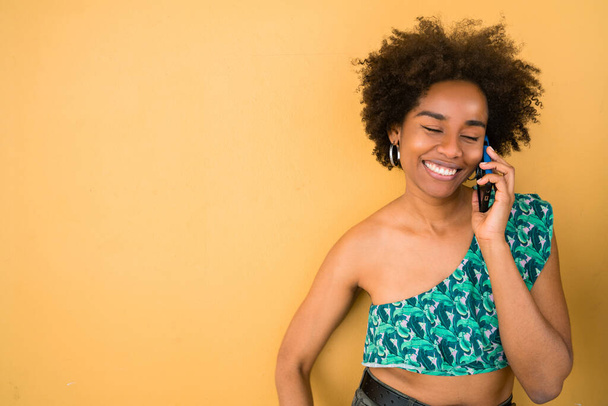 Portrait of young afro american woman talking on the phone against yellow background. Communication concept. - Foto, immagini