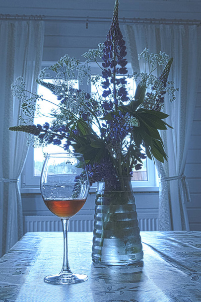A bouquet of wildflowers and a glass of wine against the background of a window in a country house - Valokuva, kuva