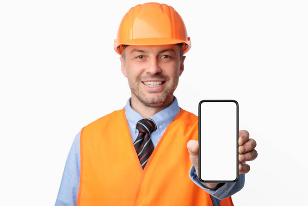 Работник строительства показывает экран мобильного телефона на белом фоне студии, макет
 - Фото, изображение
