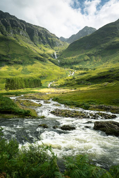 Un disparo vertical de un río rodeado de montañas y prados en Escocia. - Foto, Imagen