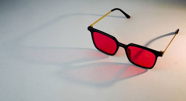 Чорно-золоті сонцезахисні окуляри з червоними лінзами на білому фоні
 - Фото, зображення