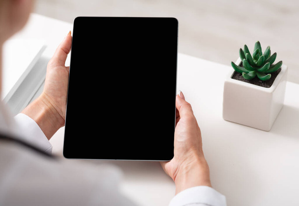 Онлайн-врач и удаленная консультация. Женщина в белом халате держит планшет с чистым экраном на белом столе в офисе
 - Фото, изображение
