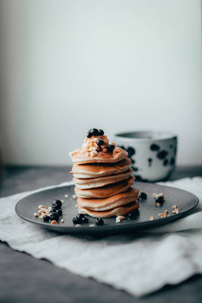 A vertical shot of tasty pancakes with syrup and berries on top on a black plate - Foto, Bild
