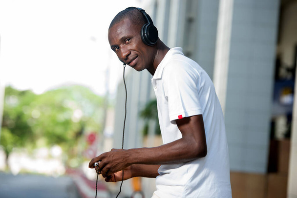 pessoas, música, tecnologia, lazer e estilo de vida - Jovem africano feliz com fones de ouvido e telefone inteligente na rua
 - Foto, Imagem