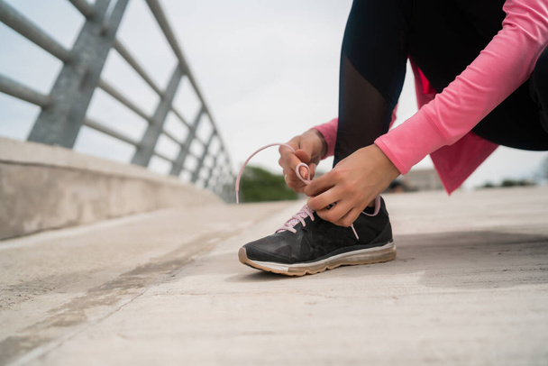 Portrait of an athletic woman  tying her shoelaces and getting ready for jogging outdoors. Sport and healthy lifestyle concept. - 写真・画像