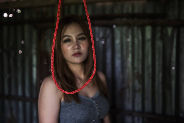 Nahaufnahme Selbstmord hängen rote Seil mit verschwommenen traurigen Frau sieht es in verlassenem Haus. Depression, Stress, Liebeskummer, Tod und Elend. - Foto, Bild