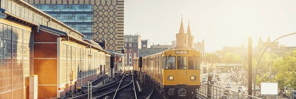 Panoramic view of Berliner U-Bahn with Oberbaum Bridge in the background in golden evening light at sunset with retro vintage Instagram style hipster filter effect, Berlin Friedrichshain-Kreuzberg - Photo, Image