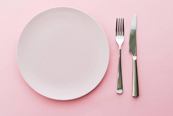 Пустая тарелка и столовые приборы как макет установлен на розовом фоне, верхняя посуда для декора стола шеф-повара и брендинг меню
 - Фото, изображение