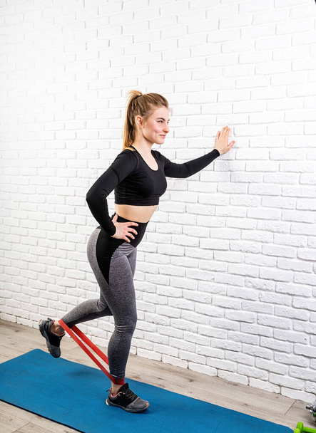 Fitness en casa. Una mujer ejercitando las piernas en casa usando goma banda de resistencia
 - Foto, imagen
