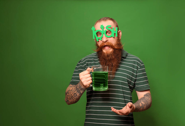 Bearded man in party glasses with green beer on color background, space for text. St. Patrick's Day celebration - Zdjęcie, obraz